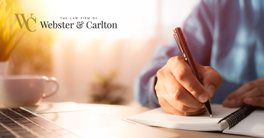 Person writing in notebook in front of laptop and mug